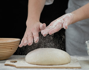 Woman sprinkl flour on a dough for cooking pastries, bread or pizza. Isolated on dark background