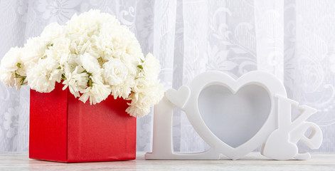 White roses in a red square box and a white photo frame close-up. Valentine's day, wedding, declaration of love. Space for text, front view, copy space.