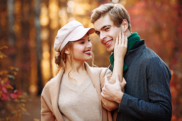 happy, couple in love hugs and smiles on the street, autumn, green scarf and cap, man and woman on a date, valentines day. walk in the park