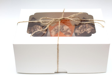 box tied with a rope with a transparent lid with chocolate cupcakes with cream top and crispy topping in paper on a white background