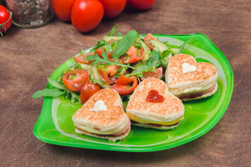 Homemade heart shaped toasts sandwiches with ham and cheese with fresh vegetable salad and arugula on a plate. Healthy vitamin breakfast cooked with love