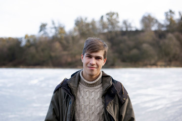 Portrait of a handsome cute guy 21-22 years old in outerwear on a background of a frozen lake