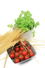 closeup of a bowl with cherry tomatoes, spaghetti and basil jar on a white background
