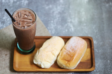 Ice chocolate fresh drink in the glass with sweet cream breads on wood tray put on stone background 