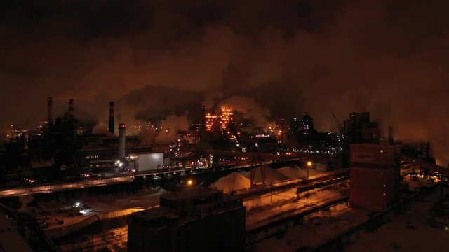 Top view of metallurgical plant blast furnace at night with smokestacks and fire blazing out of the pipe. Industrial panoramic landmark with blast furnance of metallurgical production
