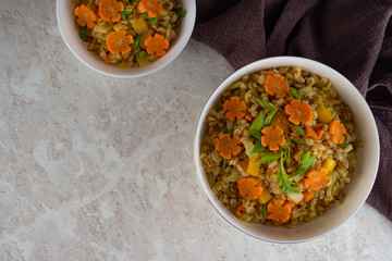 Spelt porridge in a white bowl and decorated with an asterisk carrot, diet food.