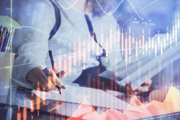 A woman hands writing information about stock market in notepad. Forex chart holograms in front. Concept of research.