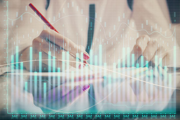 A woman hands writing information about stock market in notepad. Forex chart holograms in front. Concept of research.