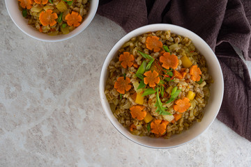 Spelt porridge in a white bowl and decorated with an asterisk carrot, diet food.