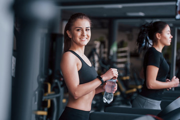Fototapeta na wymiar Two young girls in sportive clothes is in the gym together at treadmill