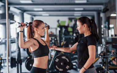 Fototapeta na wymiar Female personal trainer helping woman doing exercises in the gym