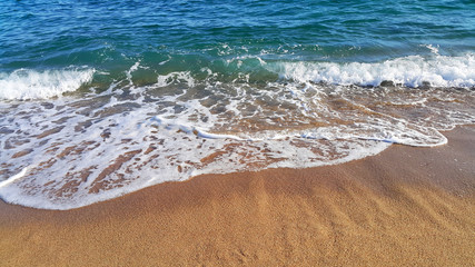 Sea wave with white foam in the coastal sand