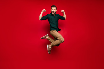 Full body photo of cheerful guy jump show his power musclar hands triceps win sport contest scream feel crazy expression wear green brown shirt sneakers isolated shine color background