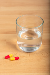 Paracetamol capsules and glass of water on a wooden table