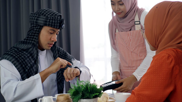 Young beautiful Asian Muslim man and women enjoying a relaxing moment in the coffee shop on a bright sunny day using mobile phone, smartwatch for mobile payment and QR code scan