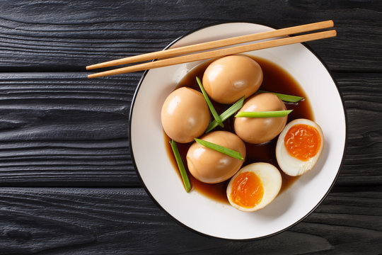Nitamago ramen boiled eggs in soya marinade with green onions close-up in a plate. Horizontal top view