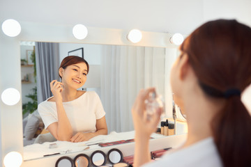 Obraz na płótnie Canvas Asian Woman applying fragrance with a spray in front of a make up mirror