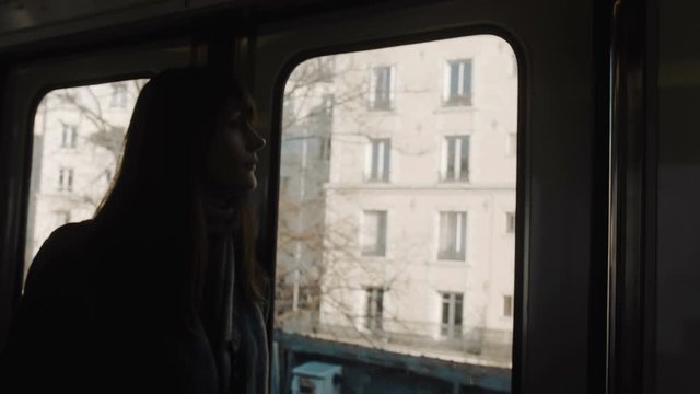 Young happy beautiful tourist woman in metro train at Paris looking at city buildings through the window slow motion.
