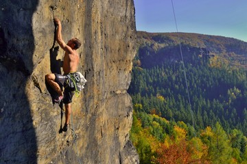 Young man is climbing on the sandstone rock in Sachsen Switzerland. Beautiful autumn day in Germany.