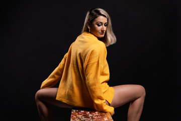 Pretty blonde girl in orange sweater posing in studio 