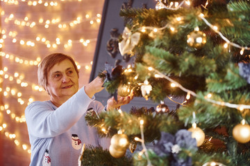 Old woman decorating christmas tree indoors in the room
