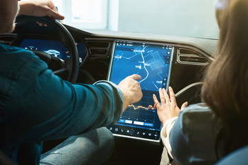 young couple man and woman checking gps navigation system in new vehicle during electric car dealership center visit