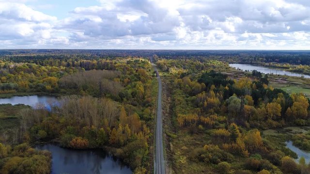 Flying over the railway in the early autumn beautiful forest and over the small river in the cloudly day.
