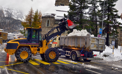 Snow cleaning tractor snow-removal machine loading pile of snow on a dump truck.