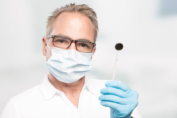 dentist with gloves and face mask holding a dental tool
