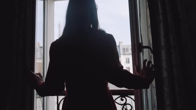 Silhouette shot of happy young local woman walking up to balcony window, enjoying sunny Eiffel Tower view slow motion.