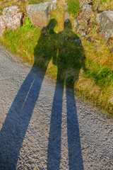 Ein Mann und eine Frau werfen einen langen Schatten auf Straße und Wiese