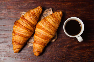 Delicious croissants and ristretto coffee in a white cup on vintage crumpled craft paper, on dark wooden tabletop