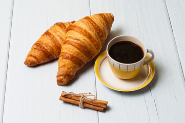 Espresso coffee in vintage yellow cup, croissants and cinnamon on a light background, breakfast concept