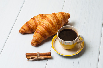 Espresso coffee in vintage yellow cup, croissants and cinnamon on a light background, breakfast concept