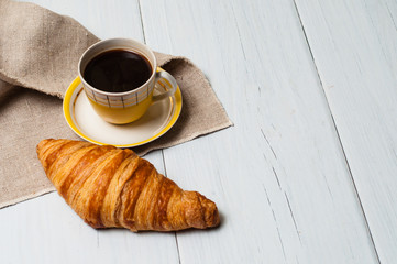 Espresso in vintage yellow cup with saucer and spoon, on linen napkin croissant on light background, concept of lunch
