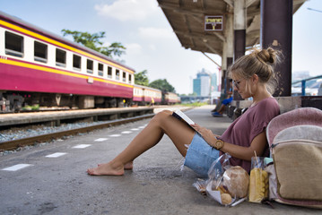 Girl with sunglasses and summer clothes sitting at a train station reading a book
