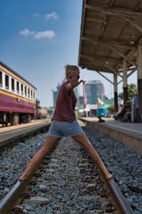 Blonde girl standing on a train track with her legs spread and one hand raised at a stop sign in the middle of a train