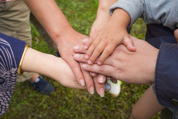 Close-up top view of young people and kid putting their hands together. Family with stack of hands showing unity and teamwork.