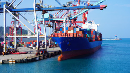 A huge container ship in the cargo terminal of an Asian port in Taiwan. Port container cranes load a moored barge with multi-colored containers. worldwide shipping by sea