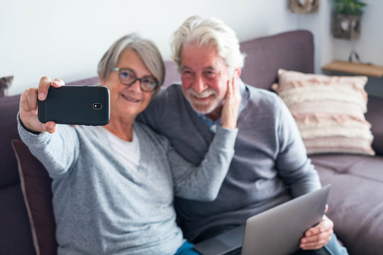 couple of two seniors or mature people on the sofa with theit laptop and taking a selfie with her phone - caucasian old people