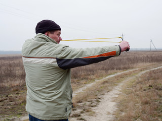 Young man shoots a slingshot in nature