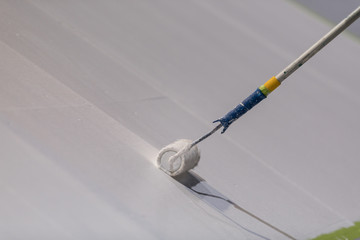 Painting a large surface white with a paint roller on a stick.