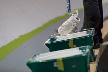 Dipping a large paint roller in a bucket with white paint to paint a large surface.