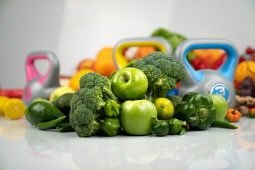 Fitness concept. Healthy nutrition: fruits and vegetables. Equipment for fitness exercises: weighing machine and dumbells. White background.