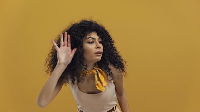 bi-racial woman eavesdropping through imaginary wall isolated on dark yellow