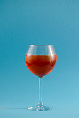 Red tropical alcohol cocktail with ice. Isolated on pastel blue background with copy space. Fruit cocktail in wine glass