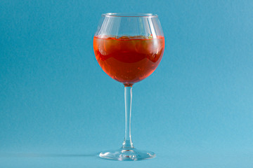 Red tropical alcohol cocktail with ice. Isolated on pastel blue background with copy space. Fruit cocktail in wine glass