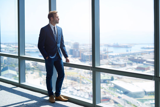 Young business achiever looking out of high office window