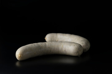 Two long white raw bratwurst sausage isolated on black background