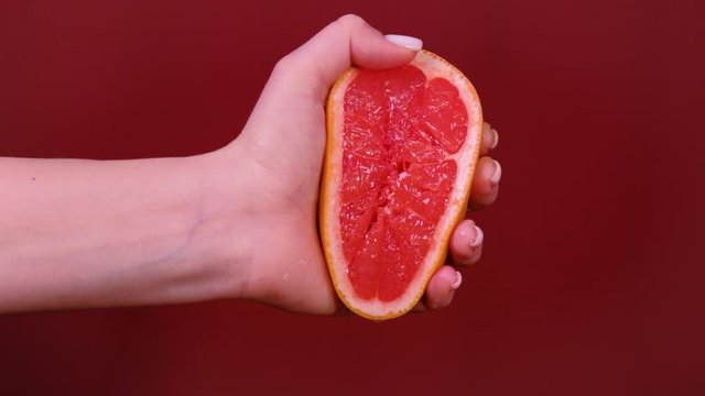 Female hand squeezing grapefruit isolated on red